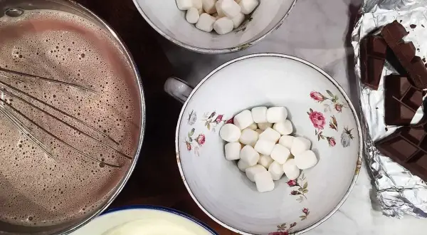 Förberedelser för en mysig stund med varm choklad. Vispad choklad i kastrull, marshmallows i skålar och chokladkakor redo att smältas.