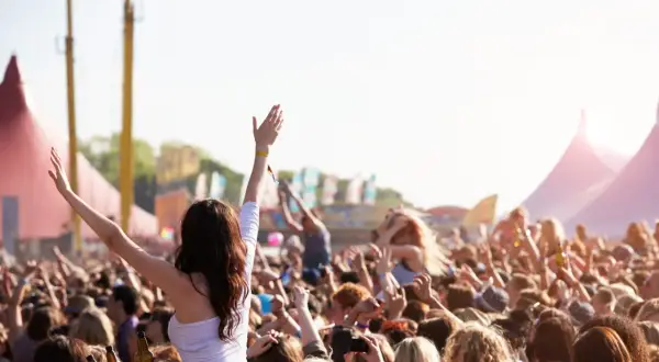 Tłum ludzi na festiwalu muzycznym, z rękami w górze, w tle namioty i sceny.