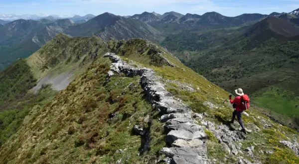 Senderista en cresta rocosa, disfrutando de vistas panorámicas de montañas verdes. Un ejemplo de las mejores rutas de senderismo en España.