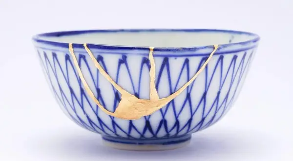 Cuenco de cerámica azul y blanco reparado con la técnica japonesa de kintsugi, resaltando las grietas con oro.