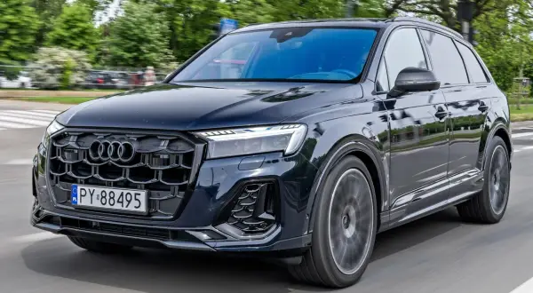 Ciemny Audi Q7 w ruchu, z widocznym grillem i reflektorami. Poznaj audi q7 dane techniczne.
