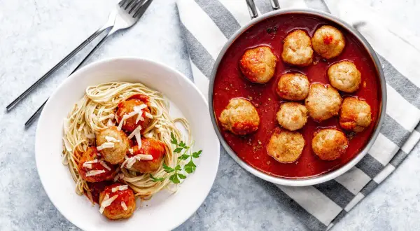 Pulpety w sosie pomidorowym na talerzu ze spaghetti i w rondelku.