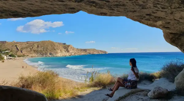 Mujer sentada en una cueva, contemplando la playa y el mar azul. Un lugar idílico que ver cerca de Cabo de Gata.