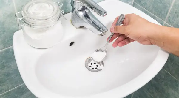 Mano versa bicarbonato nel lavandino per pulire le tubature.