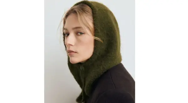 Mujer con un balaclava verde de lana, cubriendo su cabeza y cuello, con un abrigo oscuro.