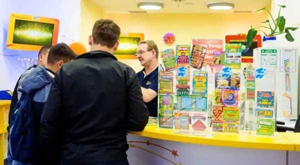 Mężczyźni stoją przy ladzie, na której widać wiele zdrapek Lotto. Czy na Orlenie są zdrapki Lotto? Tak, jak widać na zdjęciu.