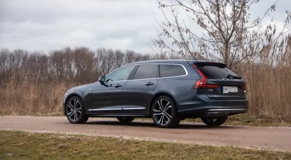 Ciemnoszary Volvo V90 T8 na drodze gruntowej, otoczony suchą trawą i drzewami.