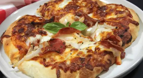Pyszna pizza z air fryera, z ciągnącym się serem, pepperoni i cebulą, ozdobiona listkiem bazylii.