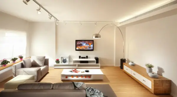Iluminar un salón moderno con focos dirigibles y una lámpara de arco. Sofás grises, mesa de centro blanca y mueble de TV.