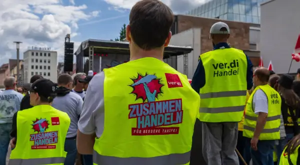 Menschen in Warnwesten mit der Aufschrift "ZUSAMMEN HANDELN FÜR BESSERE TARIFE!" bei Tarifverhandlungen im Einzelhandel.
