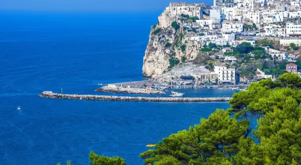 Rodi Garganico, Puglia: case bianche aggrappate alla scogliera, un porto con barche e il mare blu intenso.