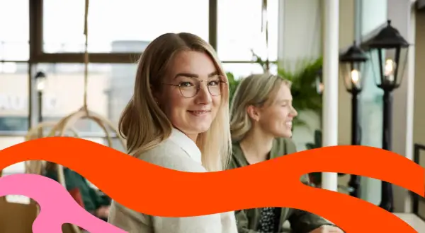 Två leende kvinnor sitter vid ett bord. Den ena tittar mot kameran. Kanske funderar de på vad som går arbetsgivaravgiften till.