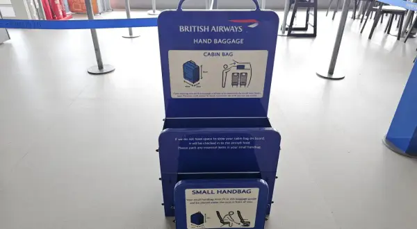 Niebieska miarka bagażu podręcznego British Airways na lotnisku. Sprawdź, czy Twój bagaż podręczny zmieści się w wyznaczonych wymiarach.