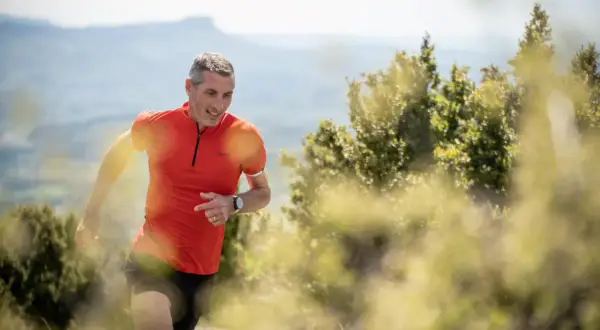 Un coureur trail en plein effort, souriant, sur un sentier de montagne ensoleillé.