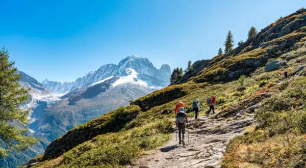 Senderismo en Francia, un grupo de excursionistas asciende por un sendero rocoso con vistas a picos nevados y un glaciar.
