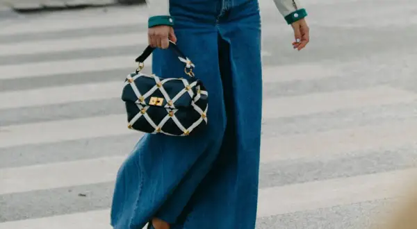 Un outfit gonna jeans lunga con borsa a tracolla trapuntata e tacchi lucidi, cammina su un attraversamento pedonale.