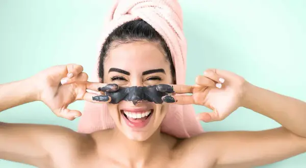 Ragazza felice con maschera viso nera, si chiede quante volte a settimana usarla per una pelle radiosa.