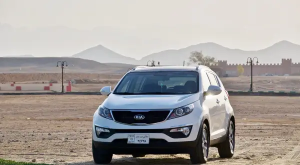 Białe Kia Sportage, jeden z popularnych modele kia, zaparkowany na pustynnym terenie z górami w tle.