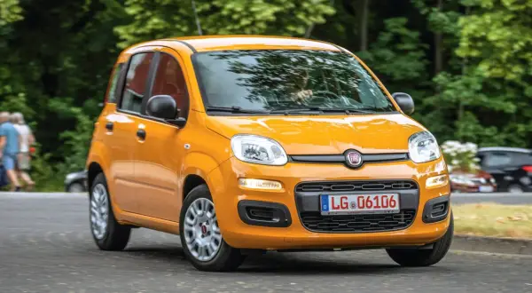 Pomarańczowy Fiat Panda 3 na drodze, z zielenią w tle.