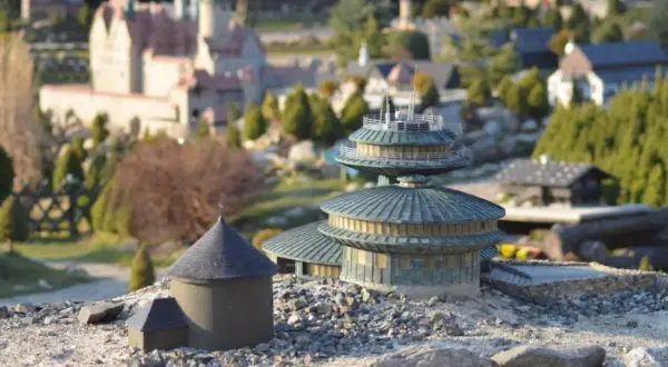 Miniaturowe budowle, w tym okrągły budynek z kopułą i wielopoziomowa konstrukcja, tworzą krajobraz jednego z parków miniatur w Polsce.