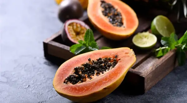 Dwa połówki papai z czarnymi nasionami, obok marakuja, limonki i mięta w drewnianej skrzynce.