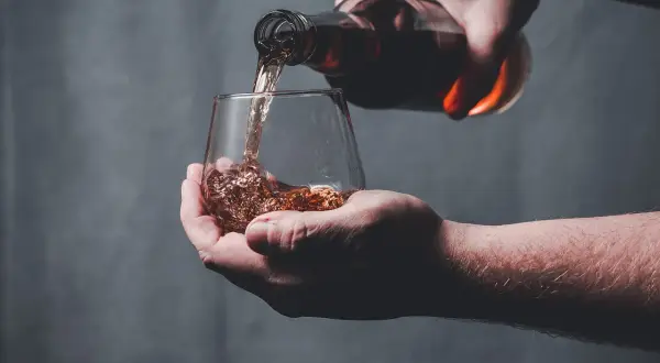 Une main verse un liquide ambré dans un verre, peut-être le pire whisky jamais goûté.