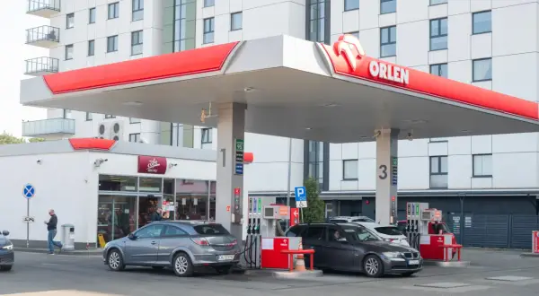 Stacja Orlen z dystrybutorami paliwa. W tle nowoczesny budynek mieszkalny. Ceny paliw, w tym akcyza, wpływają na koszty tankowania.