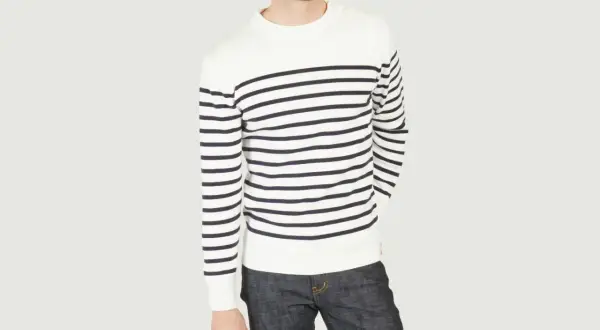Un homme porte un pull marinière marin à rayures bleues et blanches, avec un jean brut.
