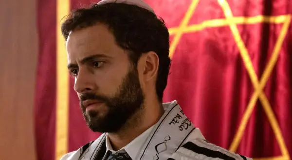 Ein Mann mit Bart und Kippa trägt einen Tallit. Im Hintergrund ist ein Davidstern auf rotem Stoff zu sehen. So sieht ein Jude aus.