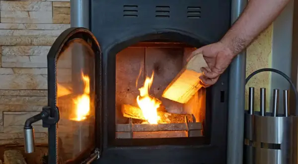 Ein Mann legt Holz in einen brennenden Kamin. Ab wann brennt Holz? Sobald es trocken ist und Zündmaterial vorhanden ist.