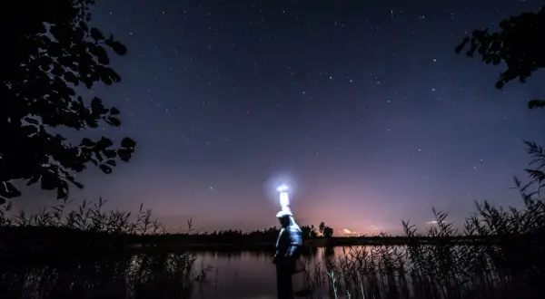 Ein Angler steht nachts im Wasser, beleuchtet von seiner Stirnlampe, unter einem sternenklaren Himmel.