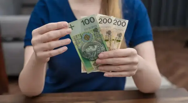 Ręce trzymają banknoty 100 i 200 zł. To wsparcie, które może pomóc w pokryciu kosztów związanych z opieką nad dzieckiem, jak zasiłek rodzicielski.