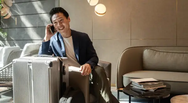 Mann telefoniert in der **Priority Pass Lounge** neben seinem silbernen Koffer. Entspannt wartet er auf seinen Flug.