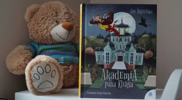 Pluszowy miś obok książki "Akademia Pana Kleksa" z ilustracją latającego Ambrożego Kleksa.