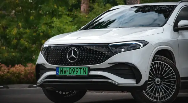 Biały Mercedes EQA z zieloną tablicą rejestracyjną WW 099TN na tle zieleni.