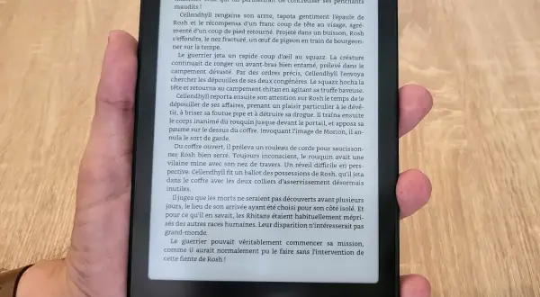 Main tenant un appareil Kindle format e-reader, affichant un texte en français sur fond noir.