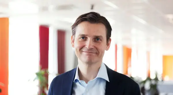 Peter Laurin, en man med blå ögon och mörkt hår, ler mot kameran i en mörkblå kavaj och ljusblå skjorta.