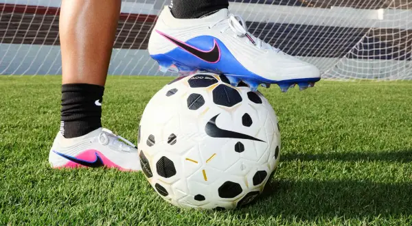 Un pied en crampons de foot, posé sur un ballon, sur l'herbe. Peut-on laver des chaussures de foot en machine ?