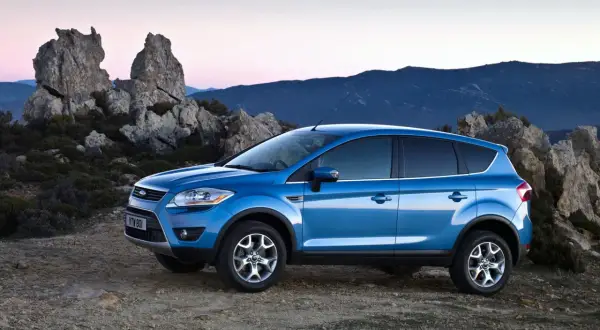 Niebieski Ford Kuga MK1 na tle skalistego krajobrazu o zachodzie słońca.