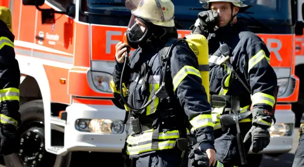 Zwei Feuerwehrmänner in voller Montur vor einem roten Feuerwehrauto. Sie sind bereit für den Einsatz. Wie viel verdient man als Feuerwehrmann?