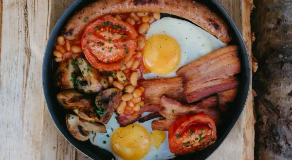 En rejäl engelsk frukost i en stekpanna: korv, ägg, bacon, bönor, tomater och champinjoner.