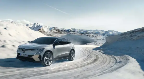 Voiture électrique avec pompe à chaleur traversant un paysage hivernal enneigé, montagnes et lac gelé en arrière-plan.