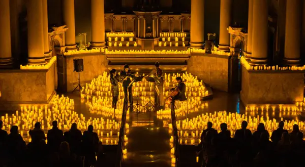 Un concierto de música clásica bajo miles de velas en Pamplona. La luz dorada de la candlelight ilumina a los músicos y al público.