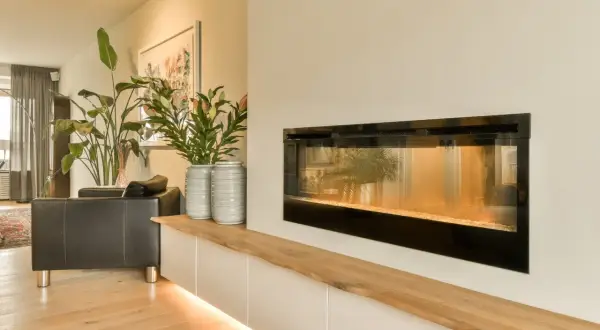 Nowoczesny biokominek w salonie inspiracje: czarna skórzana kanapa, wysokie rośliny i minimalistyczna zabudowa tworzą przytulną atmosferę.