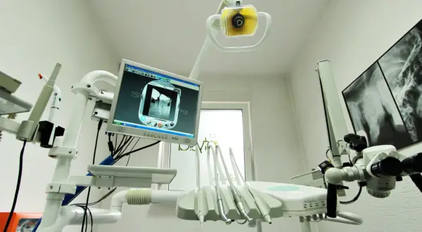 Nowoczesny gabinet stomatologiczny z aparaturą RTG i monitorem wyświetlającym zdjęcie zęba. NZOZ to skrót od Niepubliczny Zakład Opieki Zdrowotnej.