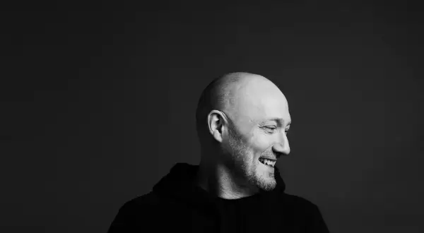 Uśmiechnięty Paul Kalkbrenner w czarnej bluzie, gotowy na koncert w Warszawie.