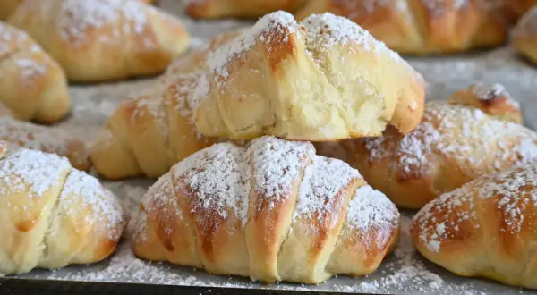 Brioches fatte in casa, dorate e soffici, cosparse di zucchero a velo. Un profumo invitante che ricorda la colazione della domenica.