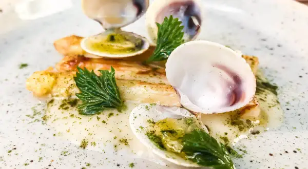 Delizioso piatto con pesce bianco, gamberi e **lupini di mare** in una salsa cremosa, guarnito con erbe fresche.