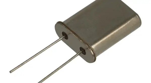 Metalowa obudowa z dwoma pinami, typowy rezonator kwarcowy, kluczowy element w elektronice do stabilizacji częstotliwości.