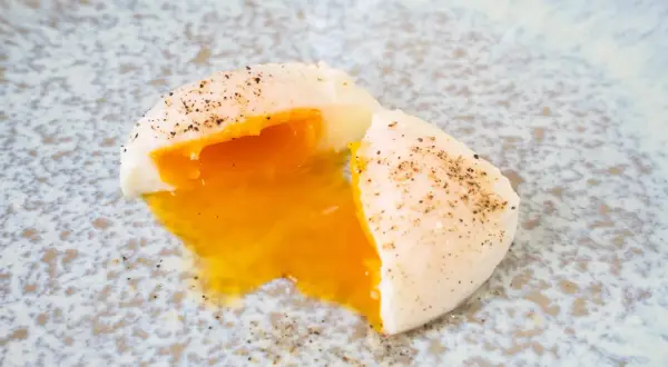 Ein perfekt pochiertes Ei mit flüssigem Eigelb, bestreut mit schwarzem Pfeffer, auf einem gemusterten Teller.